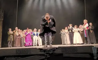 A group of performers in costume bow to an audience from a stage.