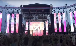 DJ stage with large screens displaying abstract pink patterns and a crowd cheering.