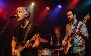 A band performs on stage with a lead singer, bassist, and drummer.