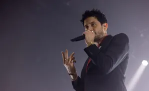 A man in a black suit and red shirt sings into a microphone, gesturing with his hands.