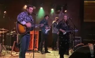 A band performs on stage, with a man singing and playing guitar at the front.