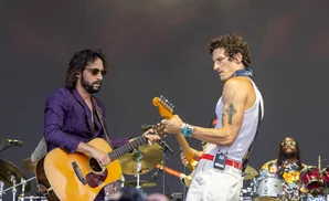 Musicians play guitar and drums on stage.