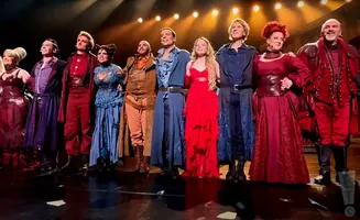 A cast of performers in colorful costumes on stage.
