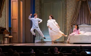 An orchestra performs on stage in a grand concert hall to a seated audience.