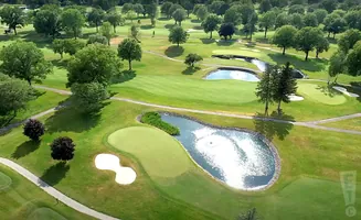 Aerial view of a golf course with manicured greens, sand traps, and water hazards surrounded by trees.