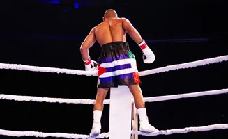 Boxer in colorful shorts and white gloves stands in a boxing ring.