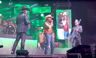 A band performs on stage with bright green screens behind them.