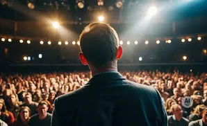 A speaker faces a large, attentive audience in a well-lit auditorium.