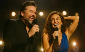 A man and a woman singing into microphones, both with joyful expressions, on a stage with soft lighting.