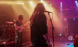 A rock band performs on a dimly lit stage with colorful spotlights.