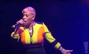 Singer with short, blonde hair wearing a colorful jacket and holding a microphone.