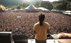 A musician with dreadlocks faces a huge crowd at an outdoor festival.