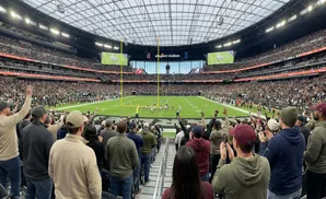 Fans cheer at Allegiant Stadium during a football game, with players on the field and a packed crowd in the stands.