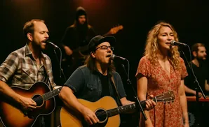 A band of three musicians perform on stage, two playing guitars and one singing.