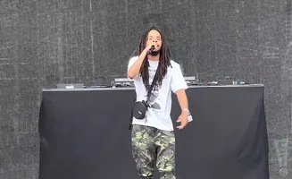 A man with dreadlocks raps into a microphone on stage.