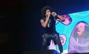 Rapper Ludacris performs on stage in a black t-shirt, leather shorts, and black leggings.