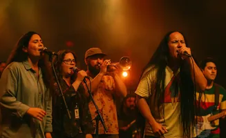A band performs on stage, with singers at microphones and a trumpet player.