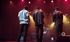 Three men on stage with red and yellow lights, facing away from the camera.