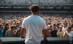 A person in a white t-shirt stands facing a large, cheering crowd in a stadium.