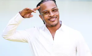 Rapper T.I. poses for a photo outdoors, wearing a white shirt and glasses.