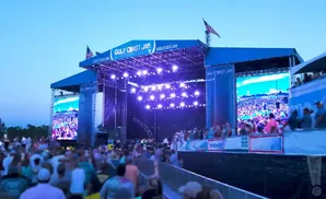 Outdoor concert stage with large screens displaying a crowd at 