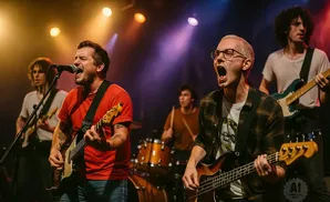 A band performs on stage. The singer in the foreground sings into a microphone while playing guitar.