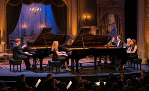 A classical piano ensemble performs on a stage with grand pianos and an orchestra.