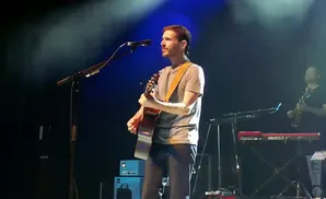 A man plays an acoustic guitar on stage with a microphone in front of him.