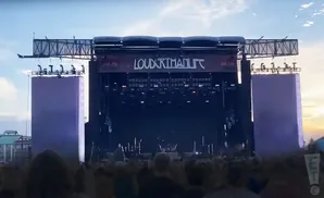 Outdoor concert stage with purple side screens and a crowd of people in the foreground.