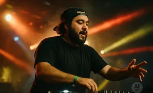 DJ with beard and black cap at a console, with stage lights in the background.