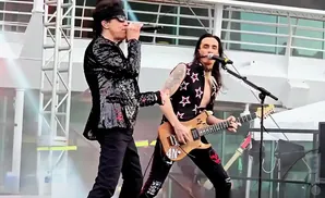 Two male musicians perform on stage; one sings into a microphone, the other plays a guitar.