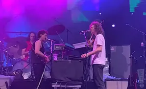 A band performs on a dimly lit stage under purple and blue lights.