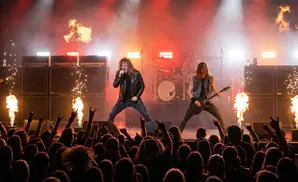 A rock band performs live with pyrotechnics and a roaring crowd.