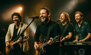 A band plays on stage, with singers and guitarists smiling and laughing.