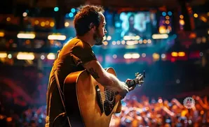 Musician playing acoustic guitar on stage with a blurred crowd and colorful lights in the background.