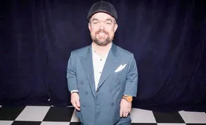 Man wearing a grey suit and cap smiles at the camera.