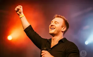 A man on stage with his fist raised, smiling with his eyes closed, holding a microphone.