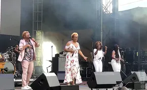 A band performs on stage, with singers in front and drums in the back.