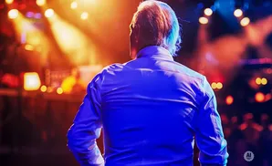 Man in a blue shirt on a stage with bright lights