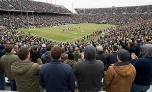 A crowd of people watch a football game from stadium seats.