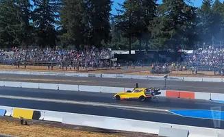 A yellow dragster speeds down a track with a crowd watching from the bleachers.