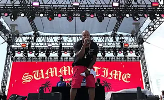 A rapper in red shorts and black shirt performs on a stage with a 