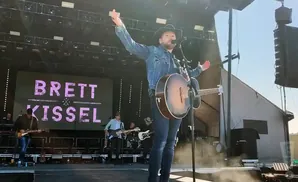 Singer Brett Kissel performs with an acoustic guitar on stage, with his name displayed on a large screen behind him.