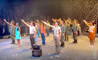A group of people on a stage with raised arms, some in military-style uniforms.