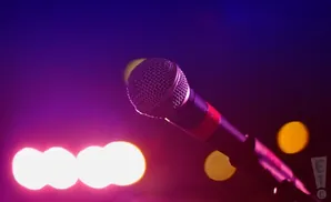 A microphone with a red band sits center stage, illuminated by purple and pink lights and blurred yellow and white orbs.