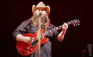 Chris Stapleton plays a red electric guitar on stage.