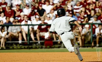Baseball player in grey uniform and black helmet runs on field with blurred crowd in background.