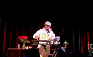 A man in a white hoodie and cap performs at a keyboard with 