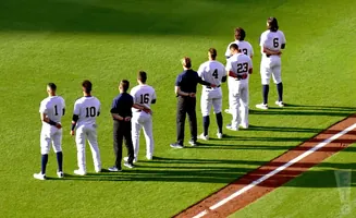 Baseball players in uniform stand on the grass field in a line.