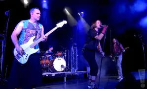 A band plays on a dimly lit stage with blue and white spotlights.